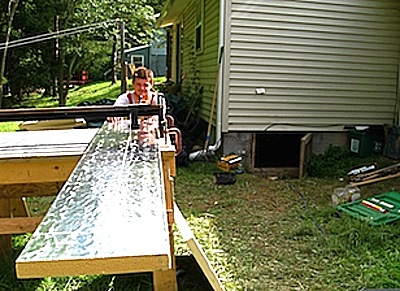 Phil Allmendinger of Snug Planet cuts another strip of insulation for the crawlspace. The soil under the Buckholtz home (at top) is very poorly drained, leading to problems with moisture and mildew invading the house. sustmpkns_snugplanet