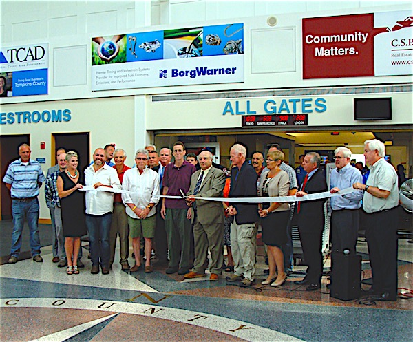 Tompkins County Legislature Chair (center) cuts the ribbon Monday as Airport Manager Mike Hall (at right of Lane) watches. They were joined by County and airport officials and local business people and representatives from the companies who are working on the runway repaving project. Runway Reopens
